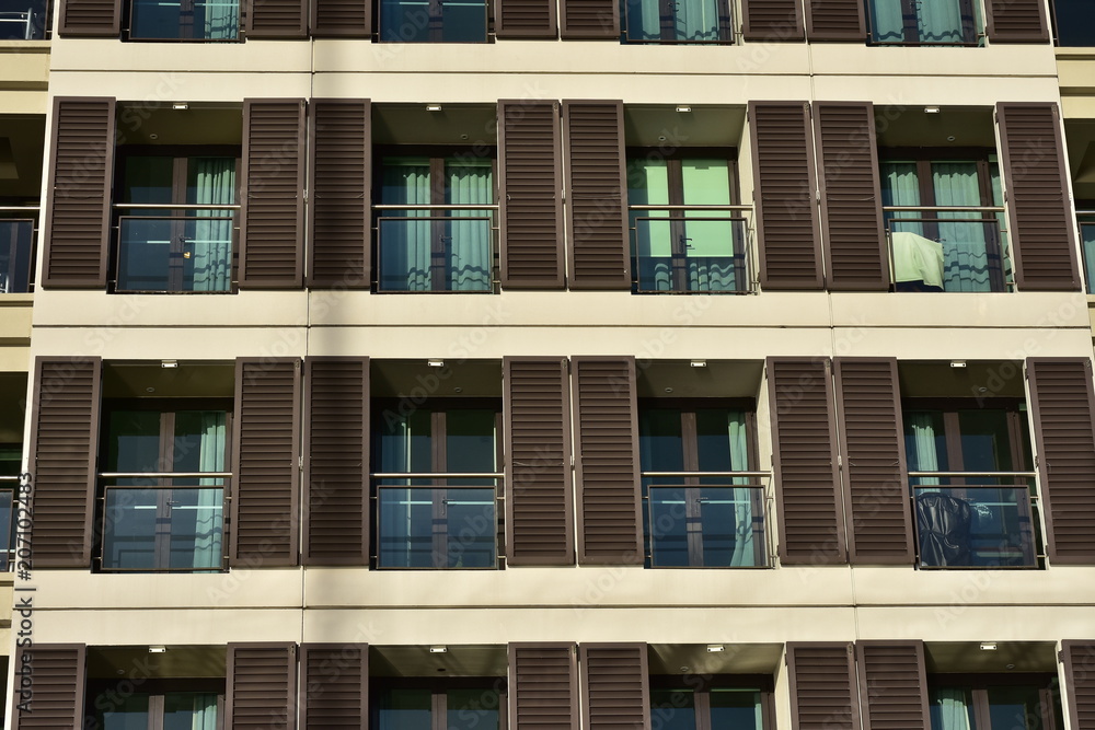 Rows of apartment balconies with glass railing and brown wooden blinds.