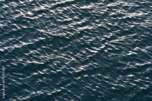 Fototapeta Dark water surface covered with small choppy waves reflecting light
