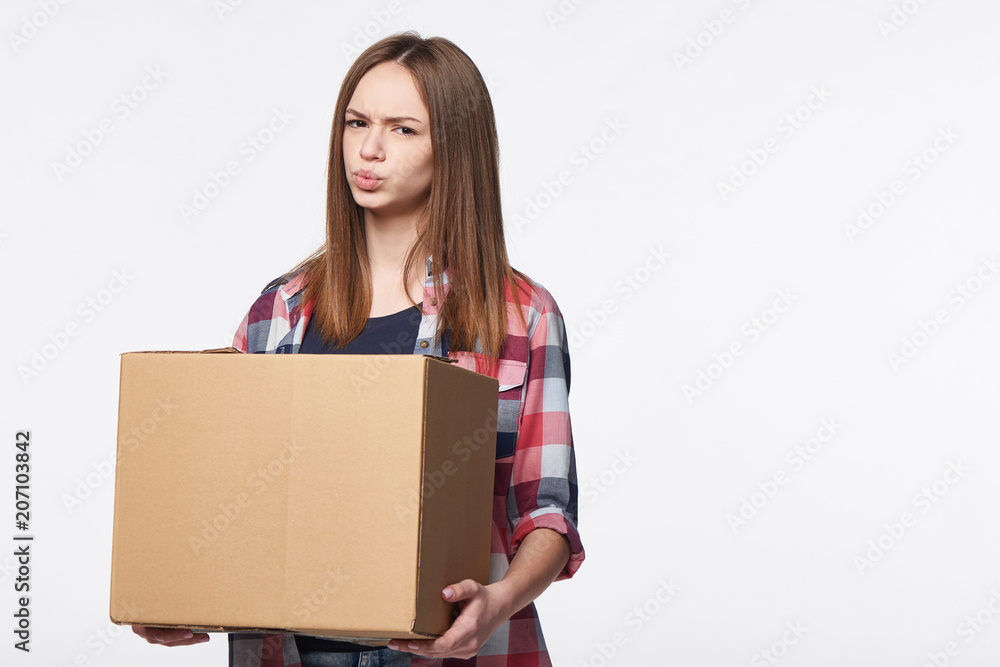 Discontent woman holding cardboard box frowning brows, over white background Discontent woman holding cardboard box frowning brows, over white background