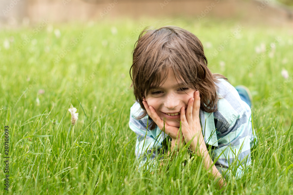 The boy blond, dressed in a blue striped shirt, lies on the grass, leaning his head on his hands, he smiles. The boy blond, dressed in a blue striped shirt, lies on the grass, leaning his head on his hands, he smiles.