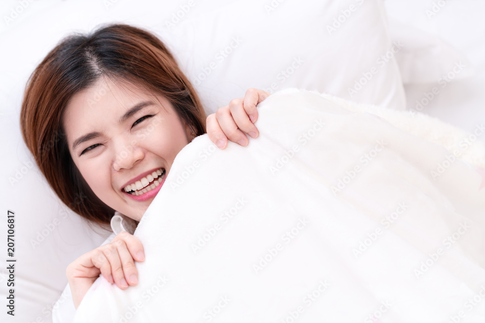 Top view of funny or enjoy young asian woman face hiding smile under blanket on bed in bedroom. Girl having fun in bed. Looking at Camera with Charming Eyes. Top view of funny or enjoy young asian woman face hiding smile under blanket on bed in bedroom. Girl having fun in bed. Looking at Camera with Charming Eyes.