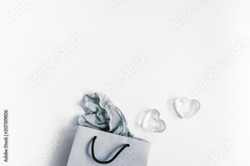 Paper bag with some clothes in it on grey background. Flatlay, top view, copy space. Shopping concept