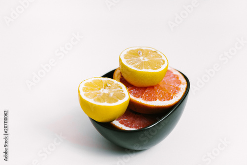 Fruit background. Colorful fresh lemons and grapefruit on a black plate on white table. Flat lay, top view, vertical orientation