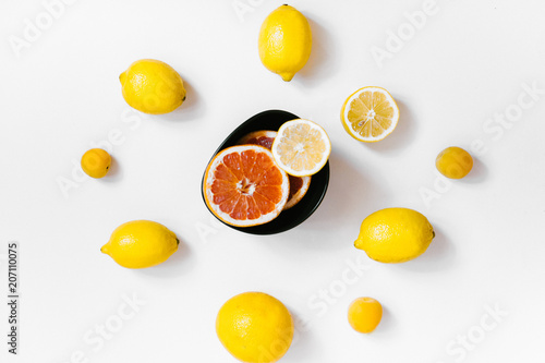 Fruit background. Colorful fresh lemons and grapefruit on a black plate on white table. Flat lay, top view, vertical orientation