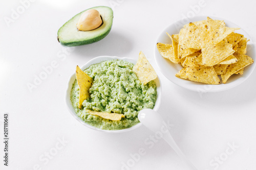 Latin American guacamole sauce with a snack of corn chips on a white table
