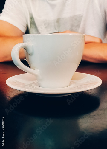 Cup of coffee on the table stands against the background of the person,