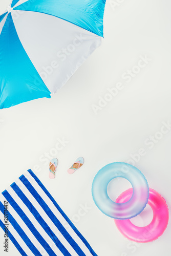 top view of beach umbrella  striped beach towel  flip flops and inflatable rings isolated on white