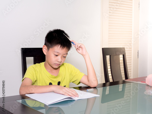 Asia little student boy studying and doing his homework at home, on the table, home education, thinking action