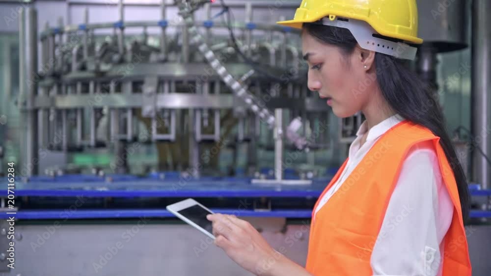 Woman industrial engineer at work in factory. Beautiful young chinese engineer working in large factory. With safety helmet and jacket. High tech automatic machine in background. Woman industrial engineer at work in factory. Beautiful young chinese engineer working in large factory. With safety helmet and jacket. High tech automatic machine in background.