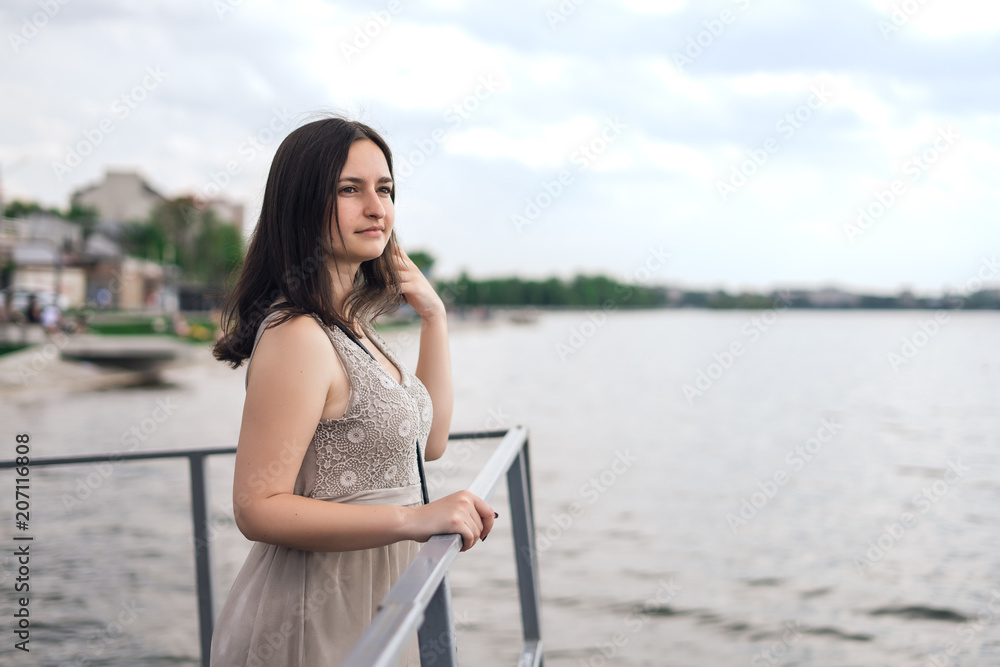 Girl is dressed at the lake. Brunette woman in gray summer dress