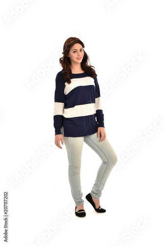 full length portrait of girl wearing striped blue and white jumper and jeans. standing pose on white studio background