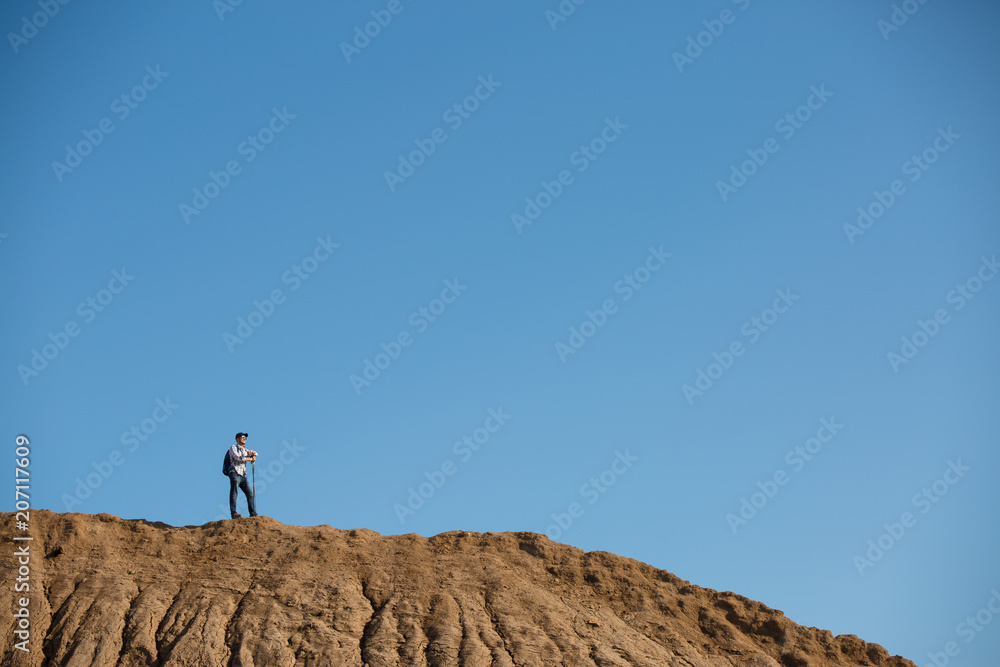 Photo of afar of male tourist with sticks for walking on hill against blue sky