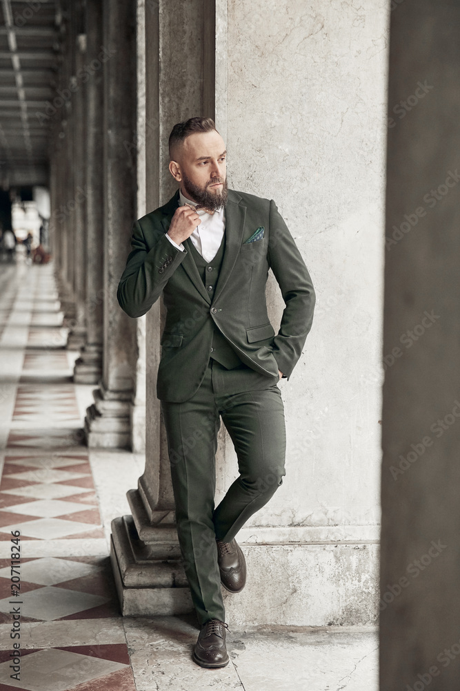 Fotka „Bearded Man In Dark Green Three-Piece Suit, Bow Tie And Brogue Shoes  Posing Near Columns In Venice, Italy“ Ze Služby Stock | Adobe Stock