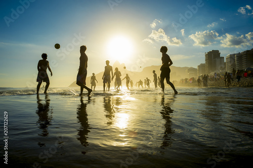 sunset silhouettes playing keepy-uppie beach football on the sea shore in Ipanema Beach Rio de Janeiro Brazil