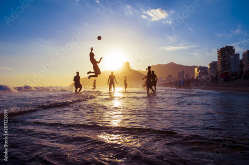 sunset silhouettes playing keepy-uppie beach football on the sea shore in Ipanema Beach Rio de Janeiro Brazil
