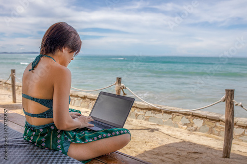 Asian woman works on laptop on the beach, work in anywhere