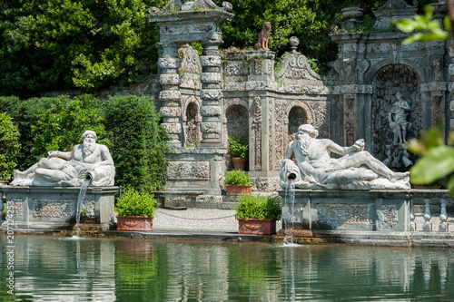Marlia, Lucca, Italy - 2018, May 25: The Villa Reale Lemon garden with large ornamental pool and stone balustrade; two statues of Giants representing the local rivers Arno and Serchio.