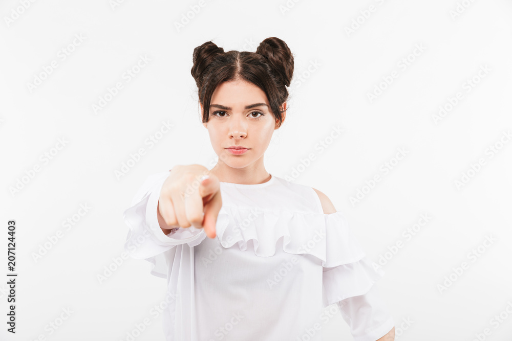 Photo of serious strict girl having double buns hairstyle pointing finger at camera with blame, isolated over white background in studio Photo of serious strict girl having double buns hairstyle pointing finger at camera with blame, isolated over white background in studio