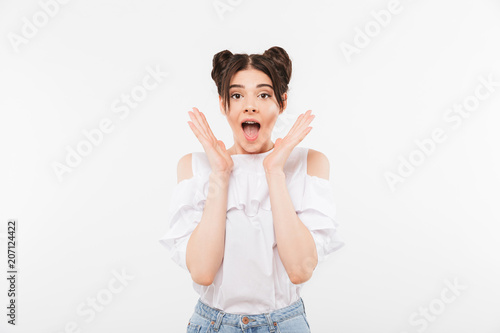 Photo closeup of excited teenage woman with double buns hairstyle and dental braces shouting in surprise or delight raising hands at face, isolated over white wall