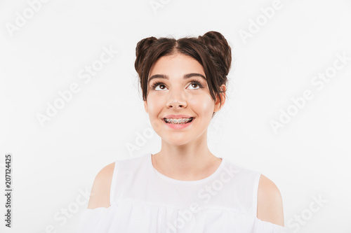 Portrait closeup of adorable teenage girl 20s with double buns hairstyle and dental braces smiling and looking upward  isolated over white background