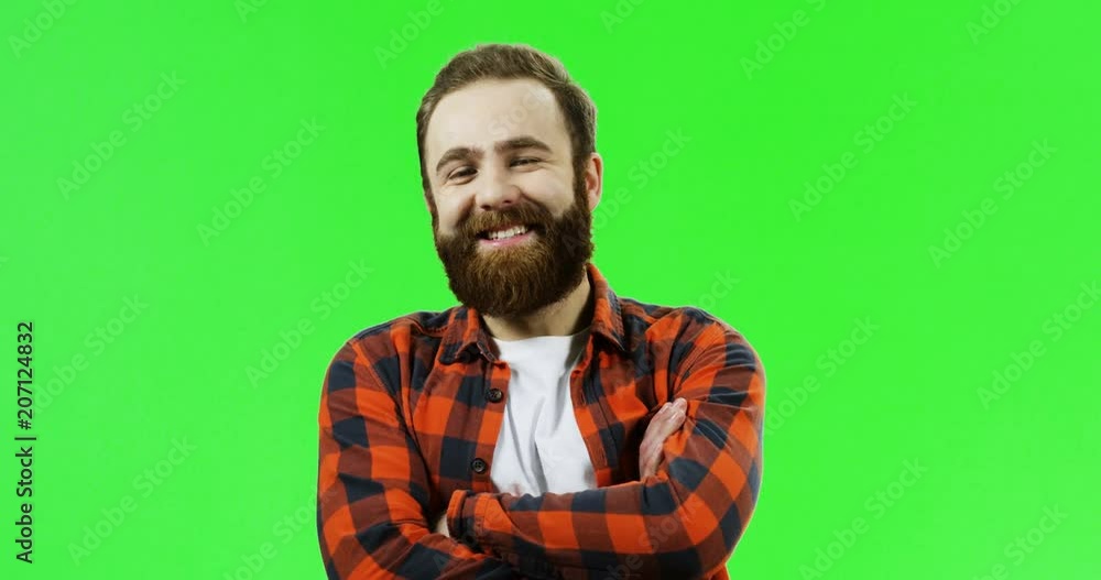 Portrait shot of the attractive caucasian man with a beard and in the red motley shirt turning to the camera with a smile and crossing his hands in front of him. Green screen. Chroma key. Portrait shot of the attractive caucasian man with a beard and in the red motley shirt turning to the camera with a smile and crossing his hands in front of him. Green screen. Chroma key.