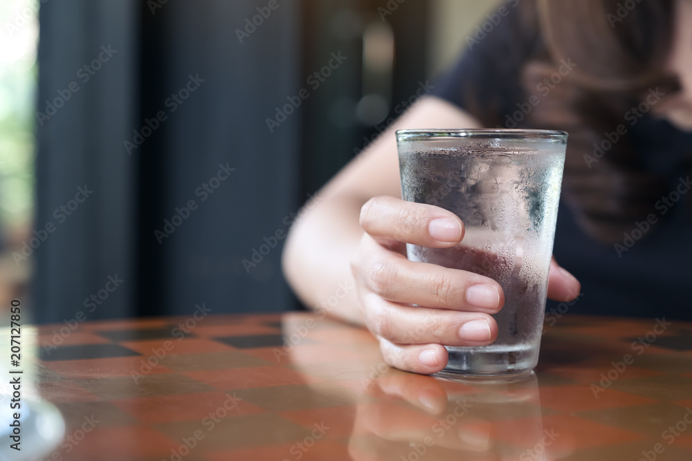 Closeup image of woman's hand holding a glass of cold water on table Closeup image of woman's hand holding a glass of cold water on table