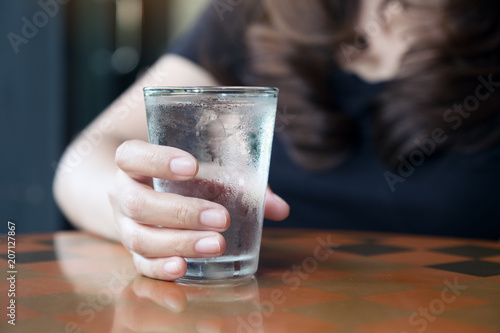 Closeup image of woman s hand holding a glass of cold water on table