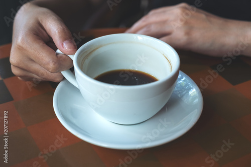 Closeup image of a hand holding and drinking hot coffee in cafe