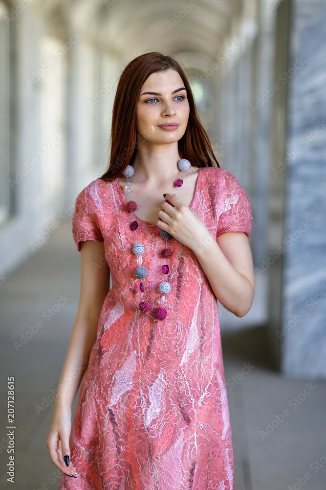 Young beautiful girl posing in seamless dress made in author's technique from merino wool in pink-peach scale, closeup