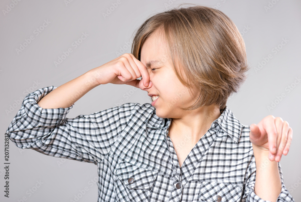 Portrait attractive caucasian girl making bad smell sign. Beautiful human face expression and emotions. Child pinching her nose, on gray background. Portrait attractive caucasian girl making bad smell sign. Beautiful human face expression and emotions. Child pinching her nose, on gray background.