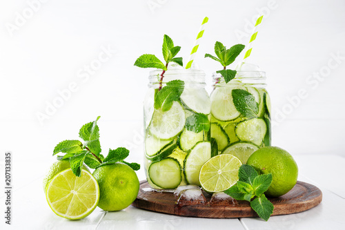 Two jars of fruit and herb infused water with cucumber, lime and mint and ice cubes on white background. The concept of detox and weight loss. Copy space