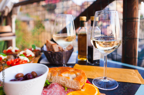 Romantic dinner for two at sunset. White wine and Tasty italian snack: fresh bruschettes  and meat on the board in outdoor cafe with amazing view in Manarola
