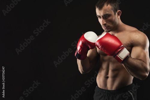 Muscular man in boxing gloves at black background © Prostock-studio