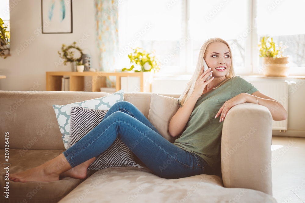 Smiling young woman talking on phone on sofa in living room Smiling young woman talking on phone on sofa in living room