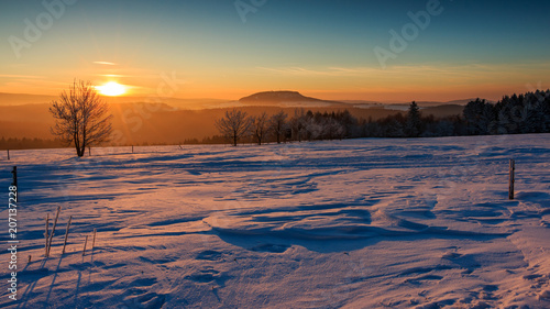 Sonnenuntergang im goldenen Sonnenlicht über dem winterlichen Erzgebirge. Blick zum Scheibenberg, Fichtelberg und Keilberg. photo