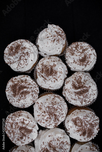 Many cupcakes on a black background. White cream and chocolate chips. View from above.