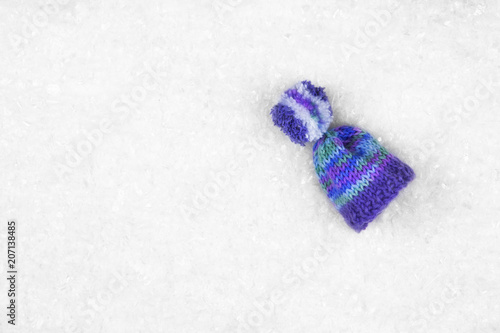 Purple wool hat/cap on the white snow with copy space. Top view.