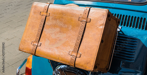 Antique brown leather case on the bridge at the bonnet flap at the back of a small car