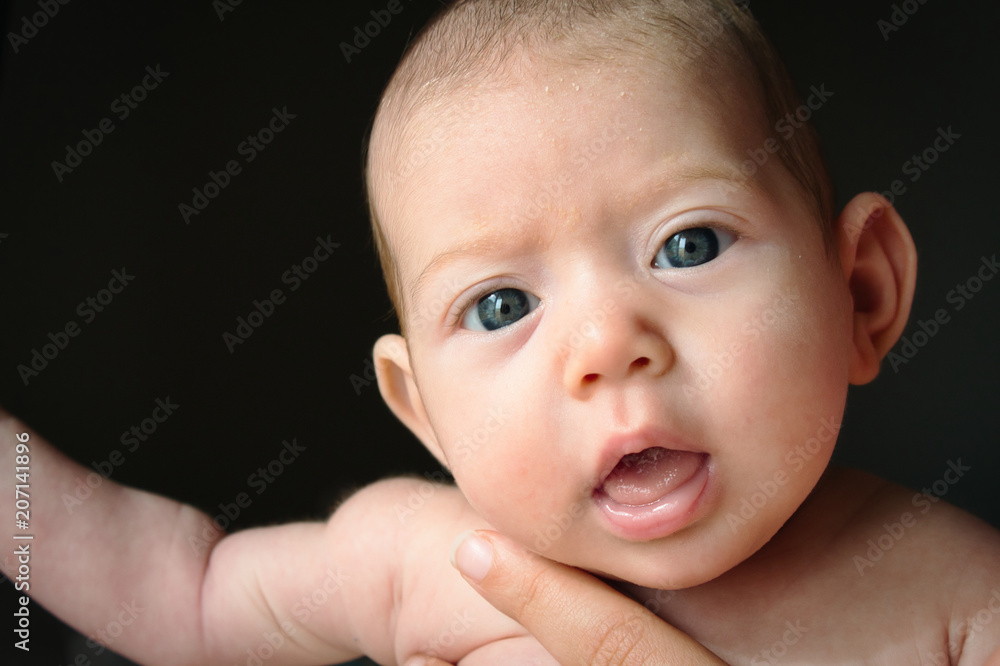 Newborn baby against black background with big eyes looking into the camera being held by her mother Newborn baby against black background with big eyes looking into the camera being held by her mother