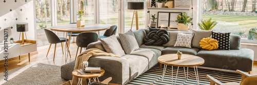 Side angle of a corner sofa with pillows, table and dining table with chairs behind in a bright living room interior photo