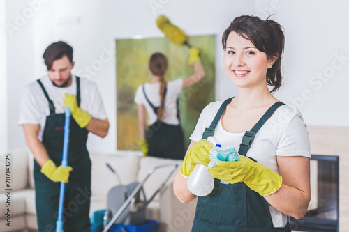 Group of young, hard-working professional cleaners in dirty apartment. Woman with cleaning solution and cloth against blurred background photo