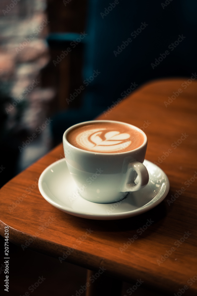 Flat white coffee latte art from above. Wooden table at the hipster coffee shop. Vintage color filter effect. Copyspace, vertical