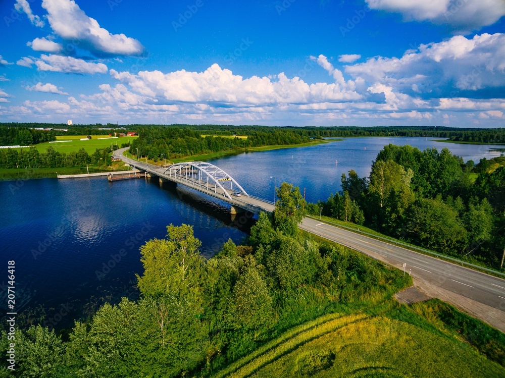 Obraz premium Aerial view on bridge over blue lake in rural Finland countryside with green and yellow fields
