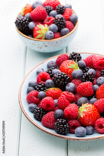 Fresh berry salad on blue dishes. Vintage wooden background.