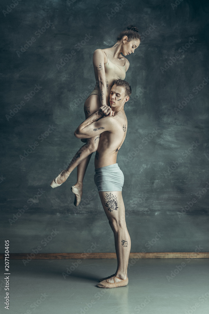 Naklejka premium The young modern ballet dancers posing on gray studio background