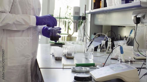 Hands of the scientist in laboratory mixing samples of the soil with water in the chemical beakers