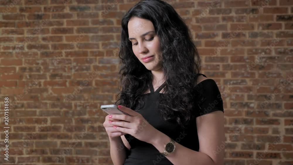 Young beautiful brunette girl is texting on her smartphone, communication concept, brick backgroung Young beautiful brunette girl is texting on her smartphone, communication concept, brick backgroung