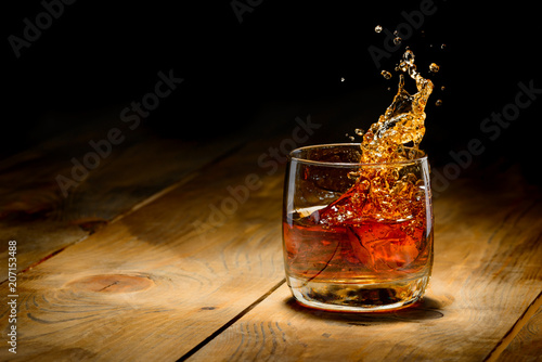 Photo Whiskey splash in glass on a wooden table.