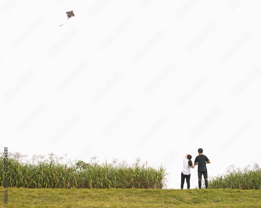 Couple flying kite during free time, standing on green grass floor with wide white sky background, empty space for text Couple flying kite during free time, standing on green grass floor with wide white sky background, empty space for text
