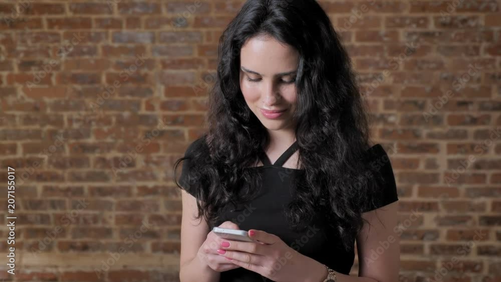 Young beautiful brunette girl surs internet on her smartphone, smiling, communication concept, brick backgroung Young beautiful brunette girl surs internet on her smartphone, smiling, communication concept, brick backgroung